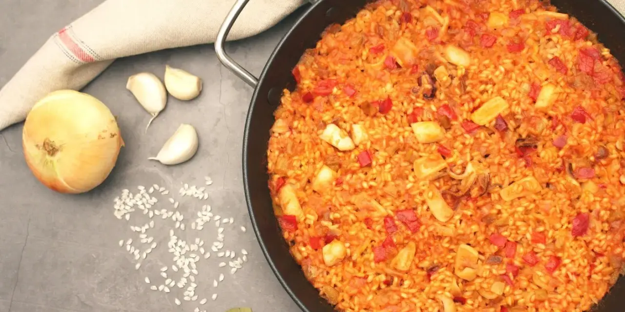 Arroz con calamares en paellera, con ingredientes como cebolla, ajo y pimientos. Un plato delicioso y lleno de sabor.