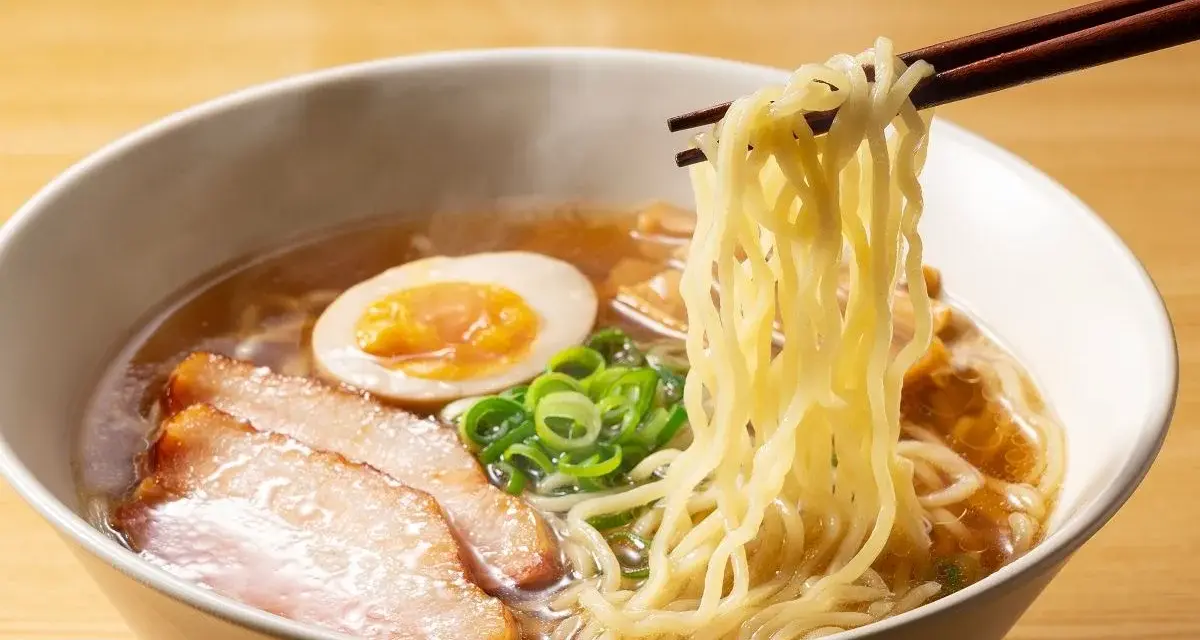 Parujące miseczka ramenu z makaronem, plastrami mięsa, jajkiem i szczypiorkiem. Idealne ramen przyprawy podkreślają smak.
