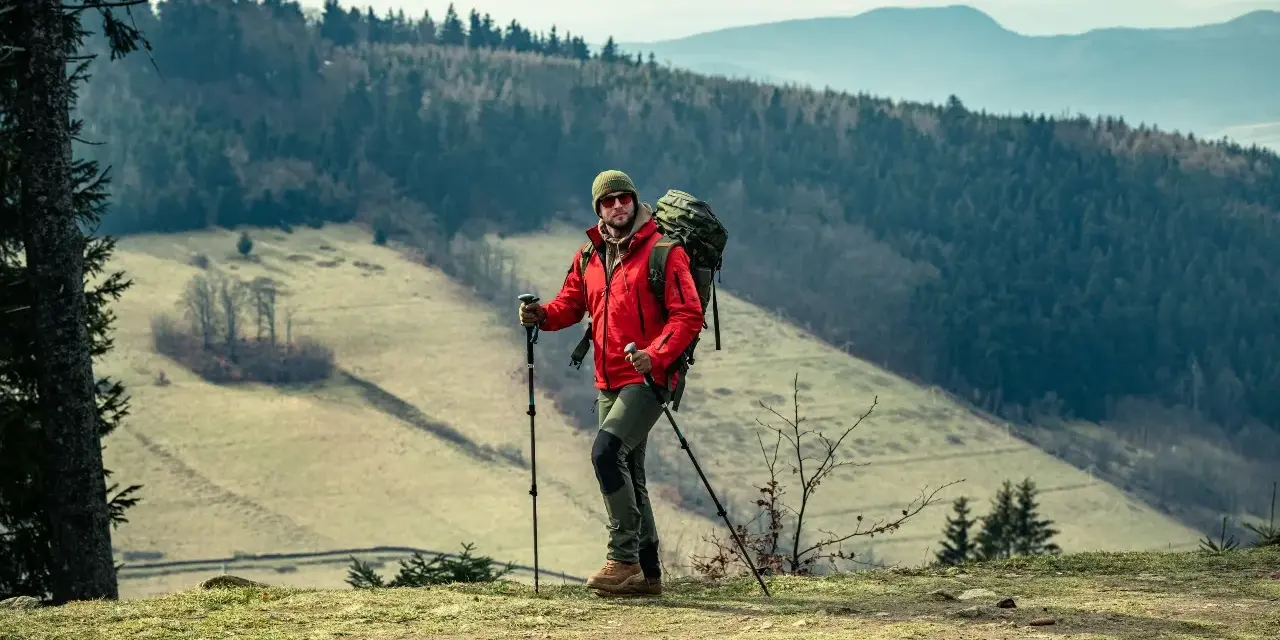 Mężczyzna w czerwonej kurtce i z plecakiem, gotowy do nordic walking. Jak zacząć? Wskazówki dla początkujących.