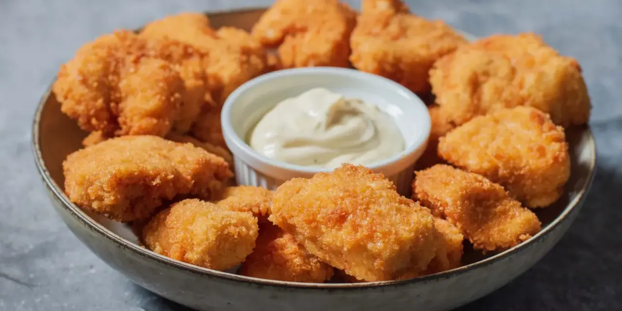 En skål med gyllene, krispiga chicken nuggets och en liten skål med krämig dippsås. Perfekt för en snabb och god måltid.
