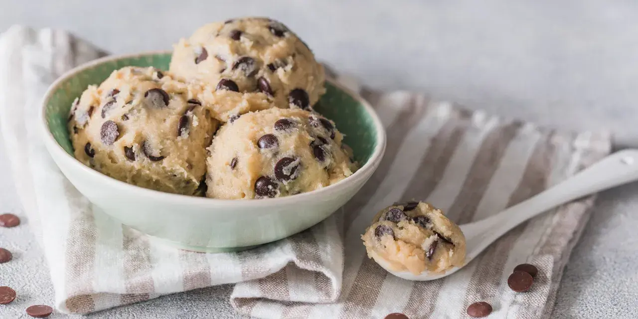 Schüssel mit köstlichem Cookie-Teig ohne Ei und Schokostückchen, bereit für den Ofen. Ein Löffel voll Teig liegt daneben.