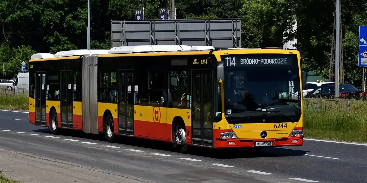 Autobus 114 jedzie ulicą w słoneczny dzień.