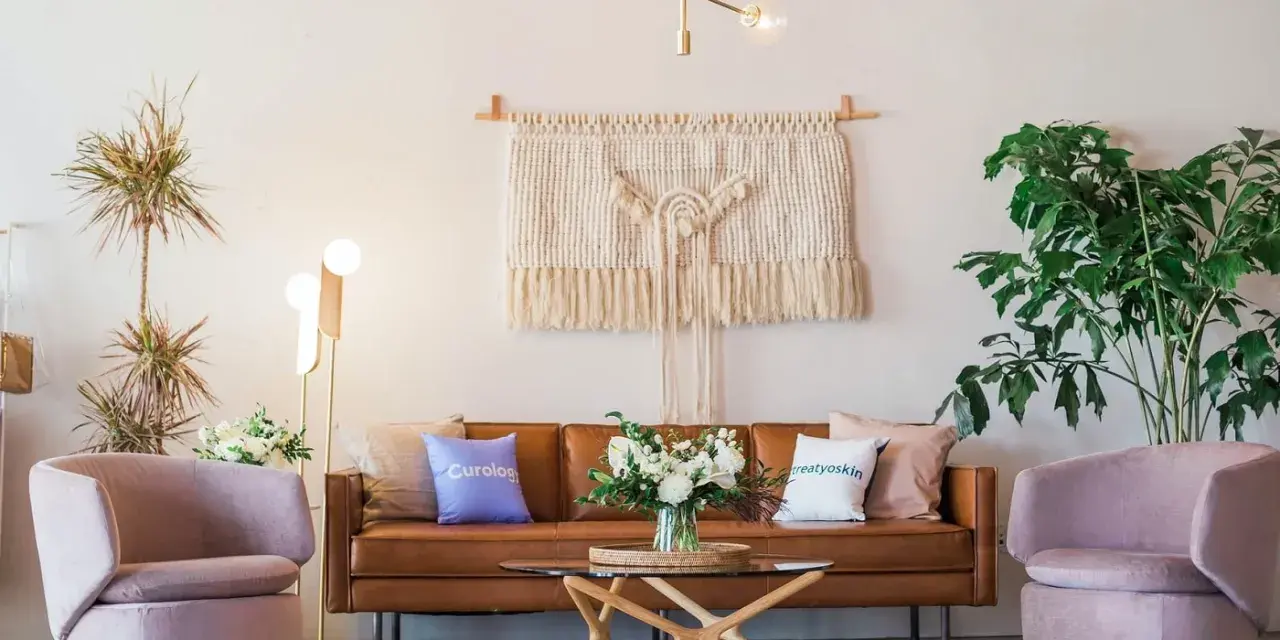 Salon moderne avec canapé en cuir marron, fauteuils roses poudrés, tapis texturé et macramé mural. La couleur peinture salon est neutre, mettant en valeur les meubles.