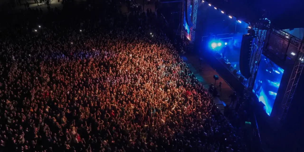 Tłum ludzi na koncercie, rozświetlony sceną i światłami. Atmosfera przed festiwalem Before Festival jest elektryzująca.