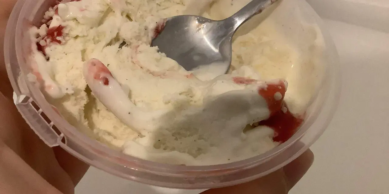 Ein Löffel steckt in einem Becher mit schmelzendem, altem Eis mit Erdbeersauce.