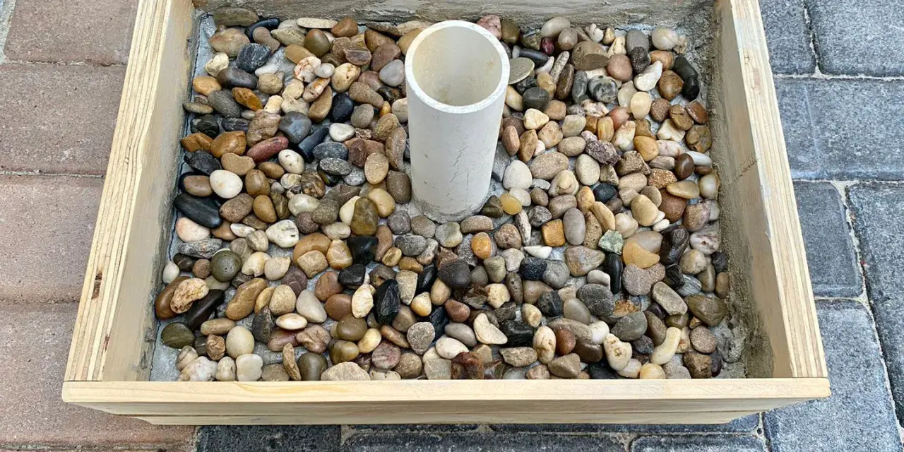 Base per ombrellone fai da te: un contenitore in legno riempito di ghiaia con un tubo centrale per l'asta.