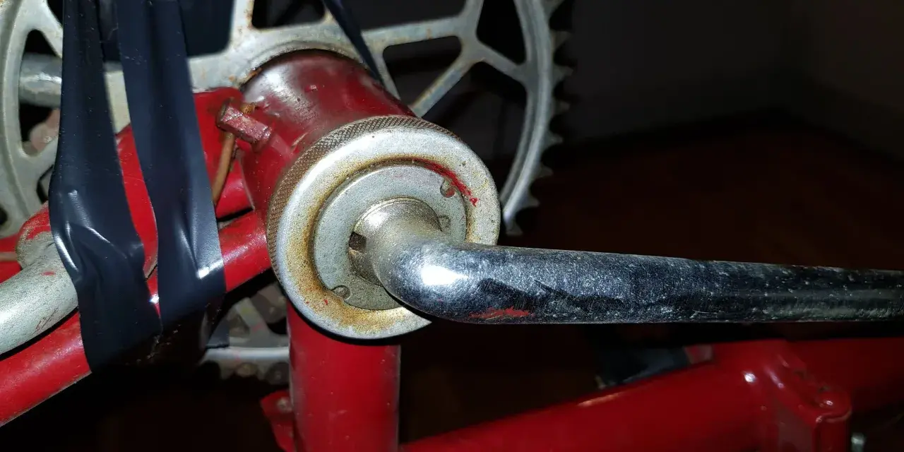 När man ska byta vevlager på cykeln syns en del av vevarmen och kedjekransen. Svart tejp håller ihop delar.
