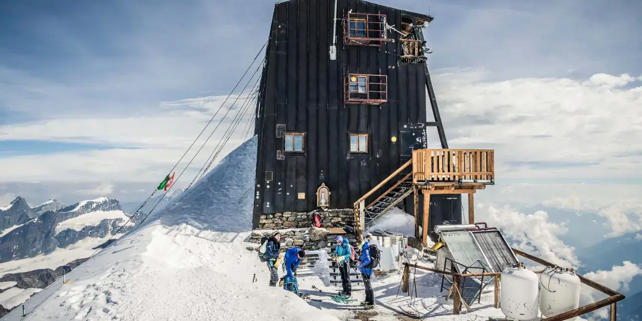 Die Capanna Margherita, eine Berghütte auf einem schneebedeckten Gipfel, mit Bergsteigern, die sich auf den Aufstieg vorbereiten.