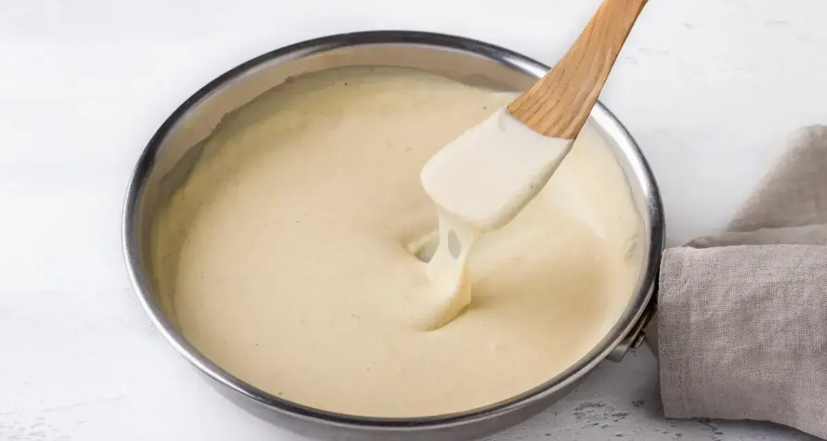 Una spatola di legno mescola una cremosa fonduta di parmigiano in una padella.