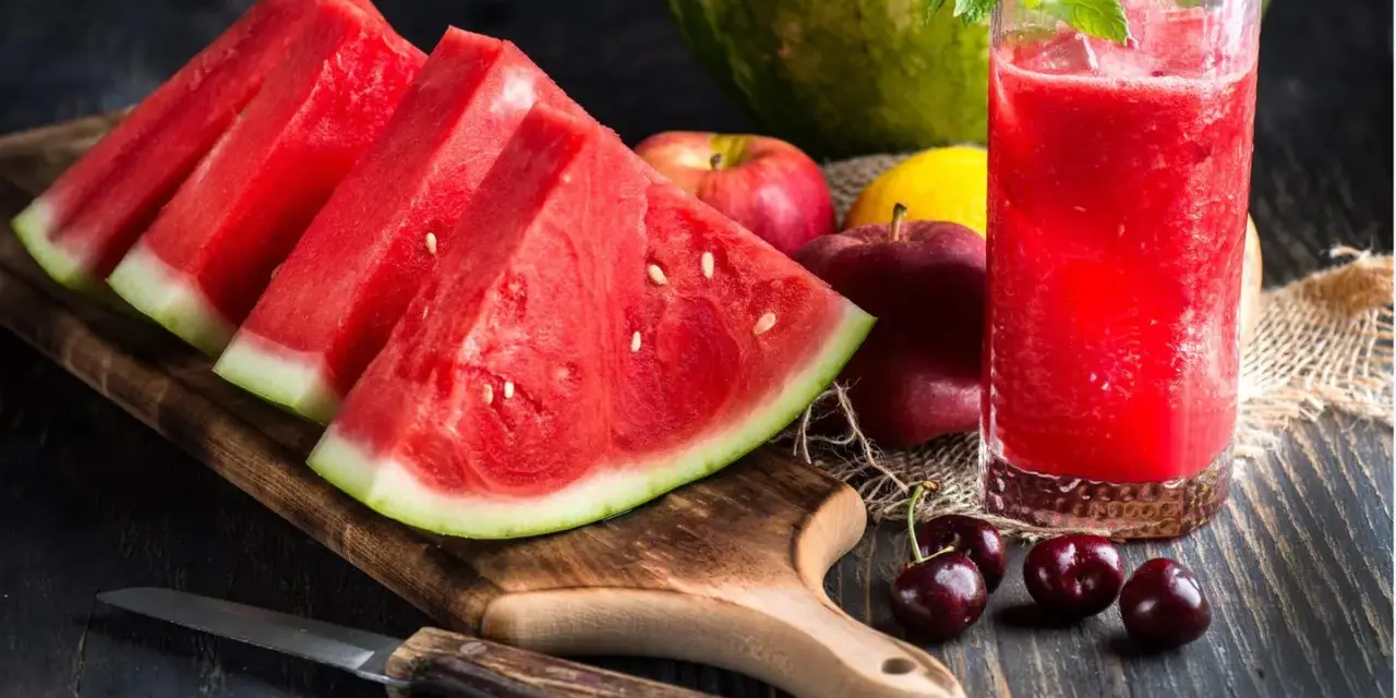 Saftige Wassermelone-Scheiben und ein Glas erfrischender Wassermelonensaft, reich an Vitaminen. Äpfel und Kirschen ergänzen das gesunde Arrangement.