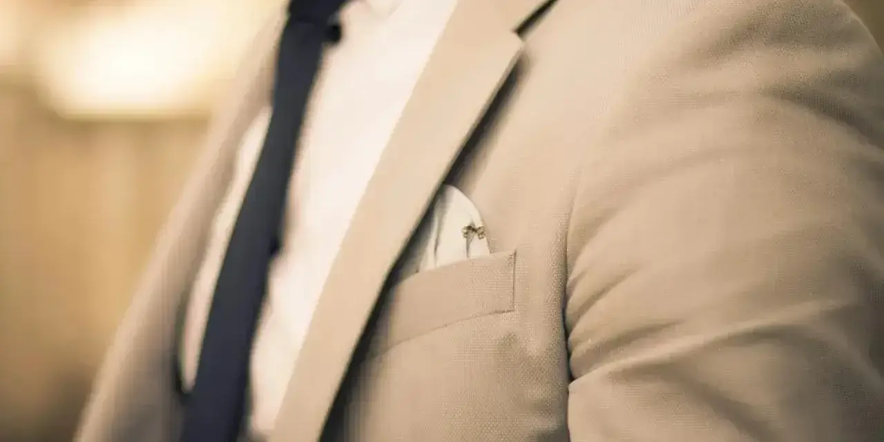Elegancki mężczyzna w jasnej marynarce i granatowym krawacie. Zastanawiasz się, ile zarabia manager hotelu?