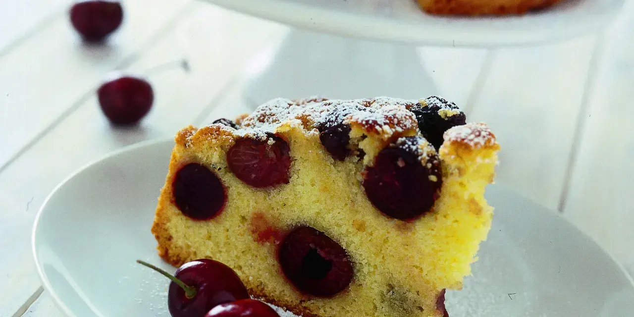 Una fetta di torta soffice e dorata, ricca di ciliegie succose, cosparsa di zucchero a velo. Perfetta per un momento di dolcezza.