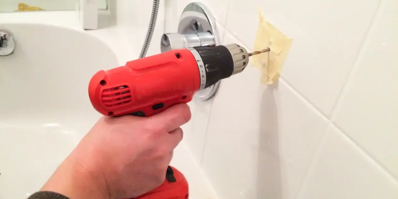 Bohren von Fliesen im Badezimmer mit einem roten Akkuschrauber. Ein Stück Klebeband schützt die Wand.