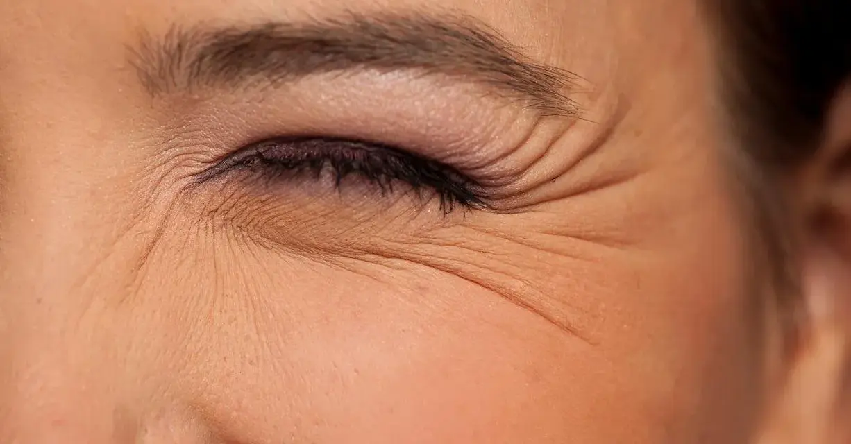 Primer plano de un ojo cerrado con maquillaje, mostrando las arrugas debajo de los ojos que marcan la expresión.