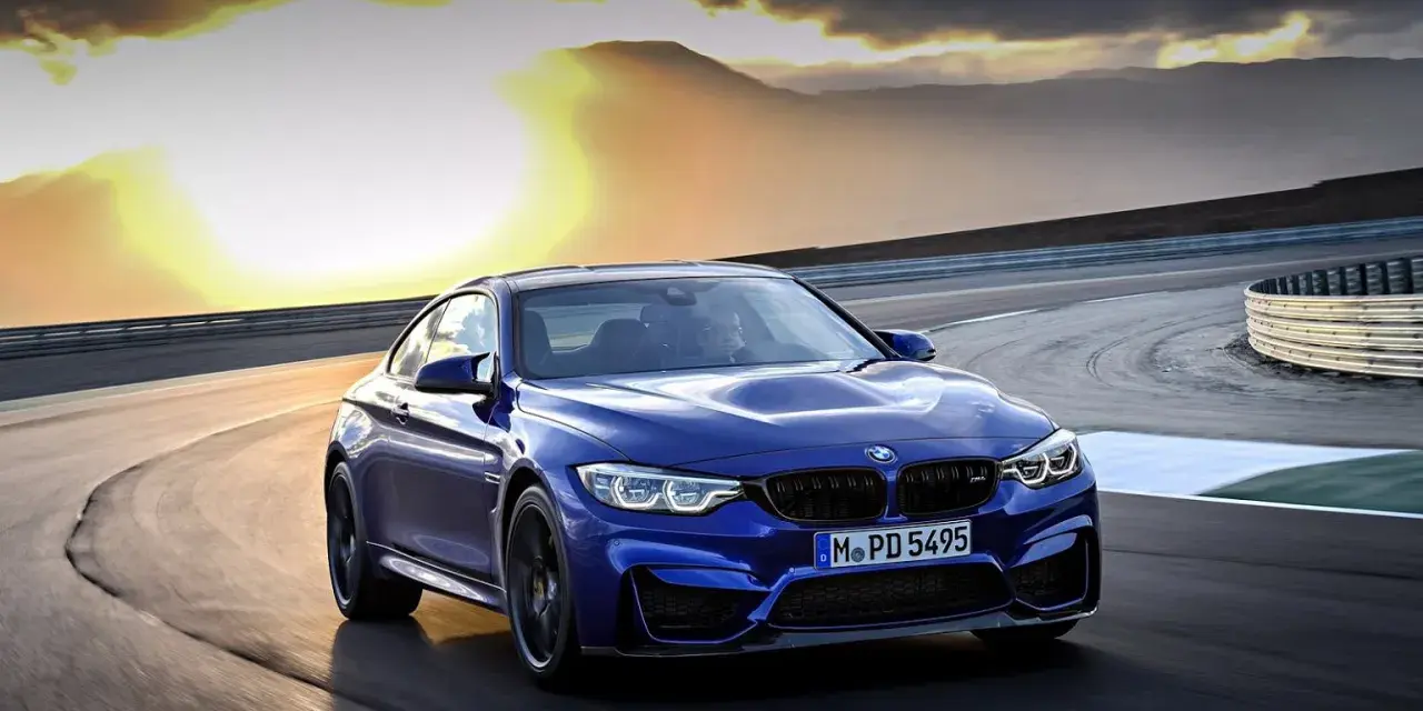Niebieskie BMW M2 CS pędzi po torze wyścigowym podczas zachodu słońca.