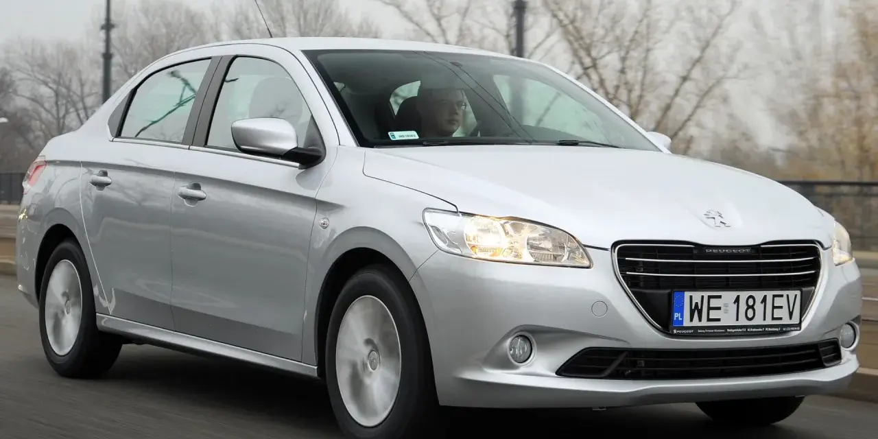 Srebrny Peugeot 301 jedzie po drodze, za kierownicą siedzi mężczyzna w okularach.
