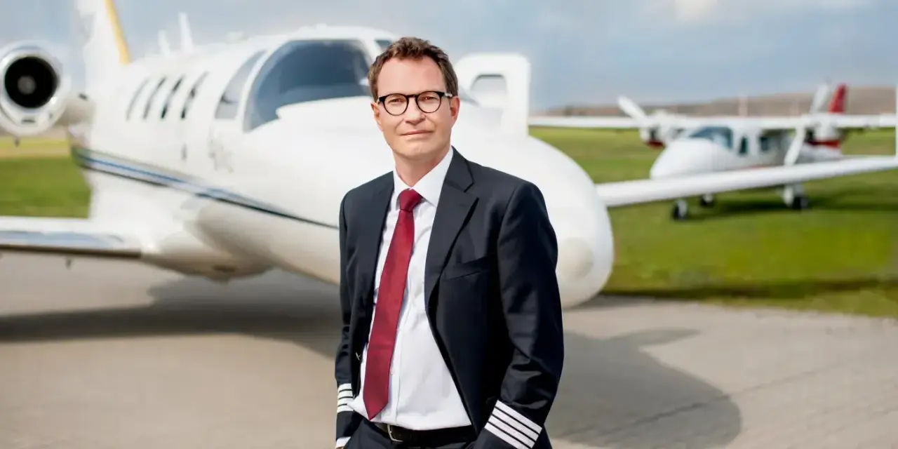 Pilot w garniturze z odznaką na rękawie, stojący przed odrzutowcem. Zastanawiasz się, ile zarabia pilot Ryanair?