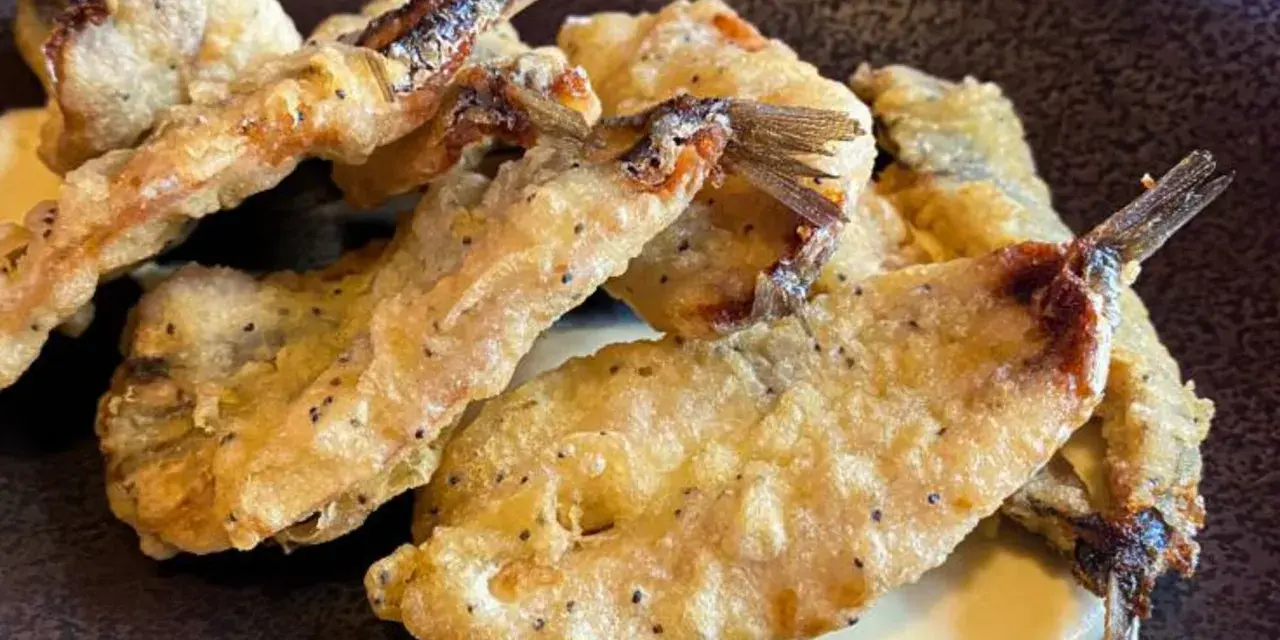 Crujientes boquerones fritos, dorados y servidos sobre una cremosa salsa.