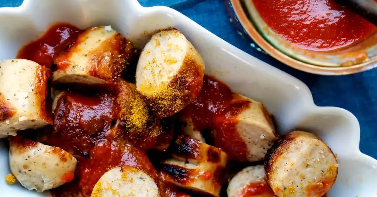 Leckere Currywurst mit einer würzigen Currywurst-Sauce und Currypulver bestreut, serviert in einer weißen Schale.
