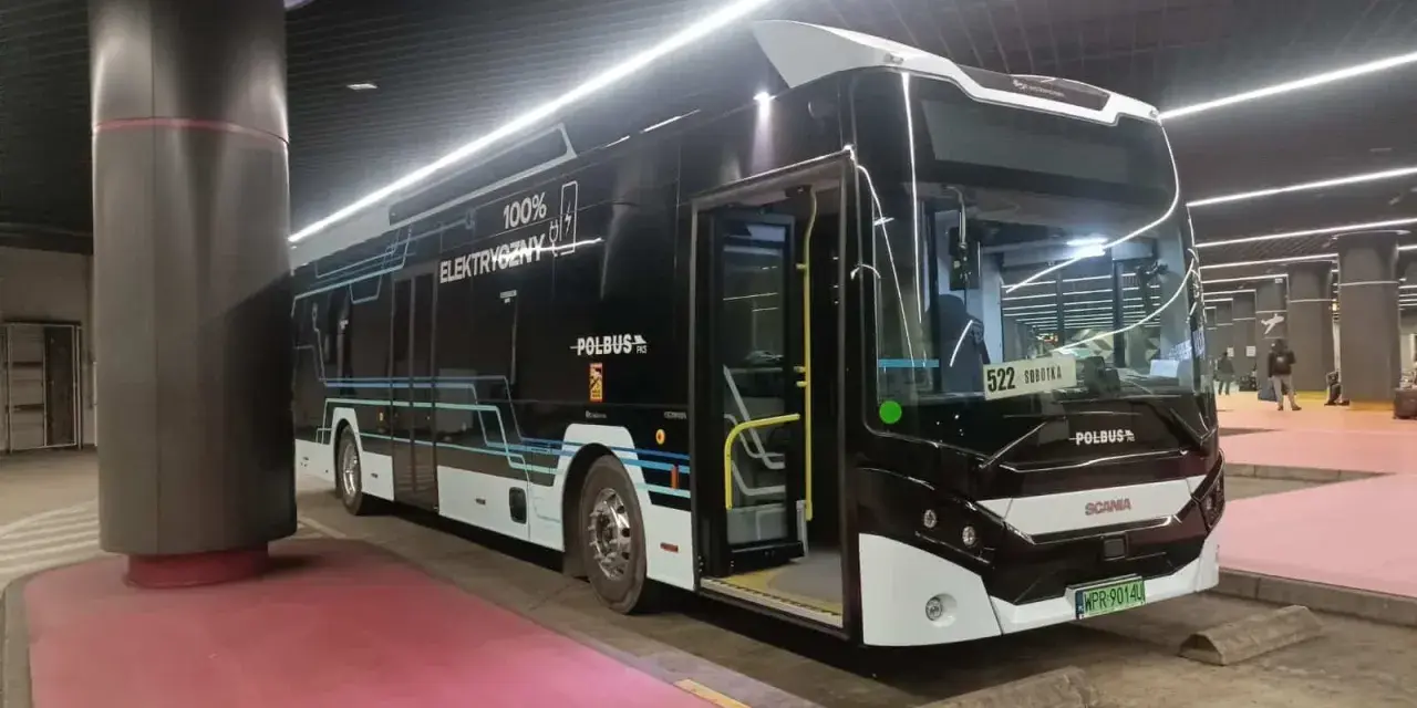 Nowoczesny, czarny autobus elektryczny z napisem "100% ELEKTRYCZNY" stoi na przystanku.
