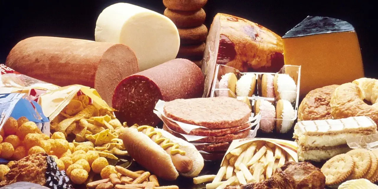 Stół ugina się pod ciężarem przetworzonej żywności: wędliny, sery, frytki, słodycze, ciastka, pączki, hamburgery i chipsy – to wszystko zawiera tłuszcze trans.