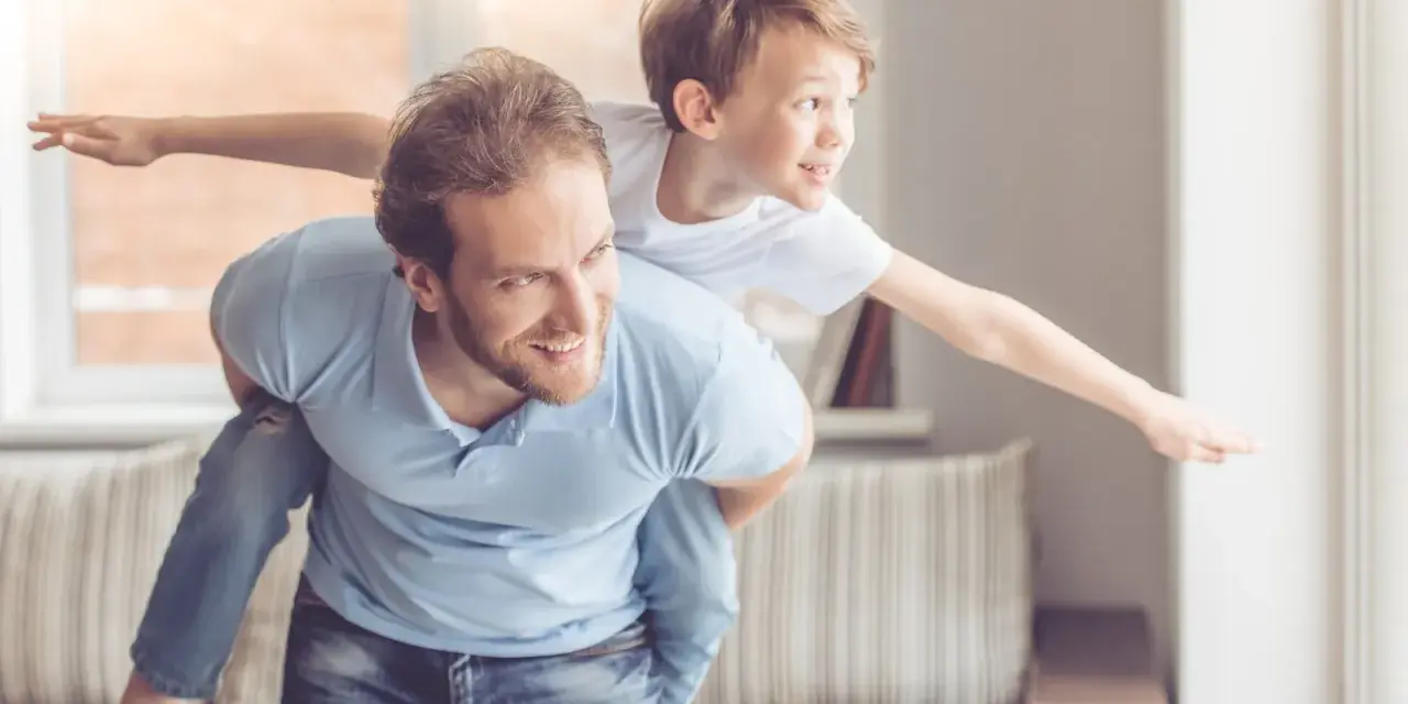 Ein Vater trägt seinen Sohn auf dem Rücken. Der Sohn streckt die Arme aus wie ein Flugzeug. Das sind meine worte an meinen sohn: Flieg hoch!