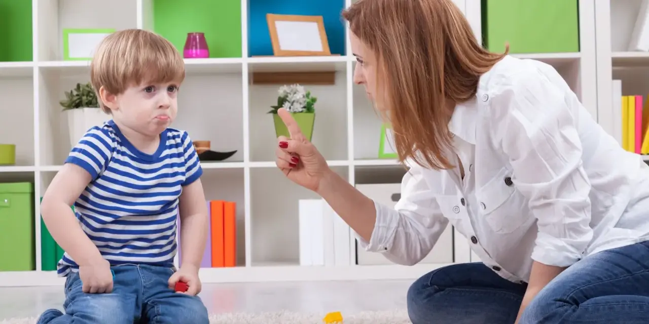 Mama karci synka za kłamstwo. Chłopiec ma smutną minę, a na dywanie leżą klocki.