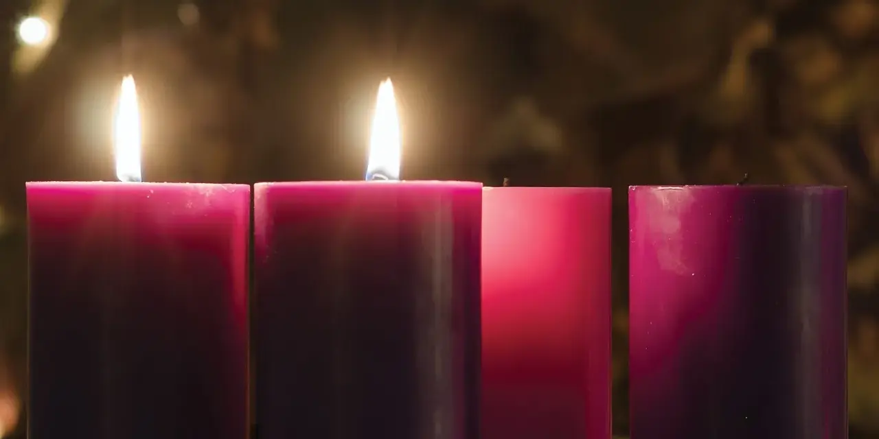 Two lit candles glow on the 2nd Sunday of Advent, their flames casting a warm light on the surrounding purple and pink candles.