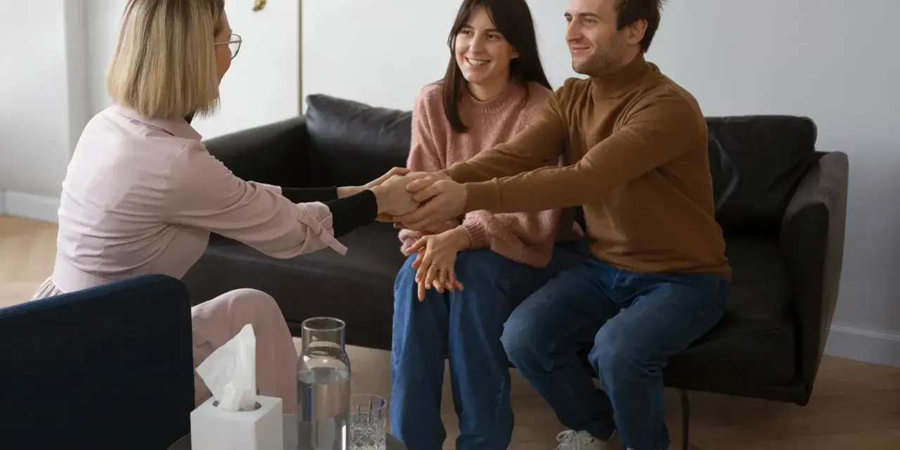 Un couple se tient la main, souriant, lors d'une séance de psychothérapie de couple avec leur thérapeute.