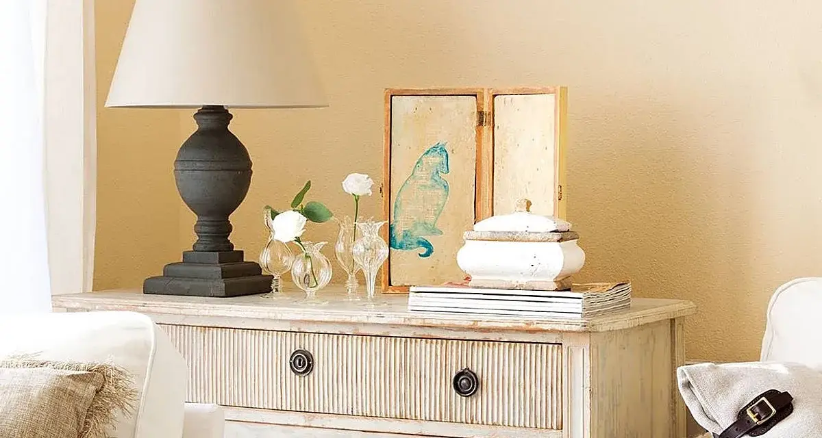 Cómoda de estilo vintage con cajones pintados a la tiza, decorada con lámpara, jarrones con flores y un cuadro de gato.