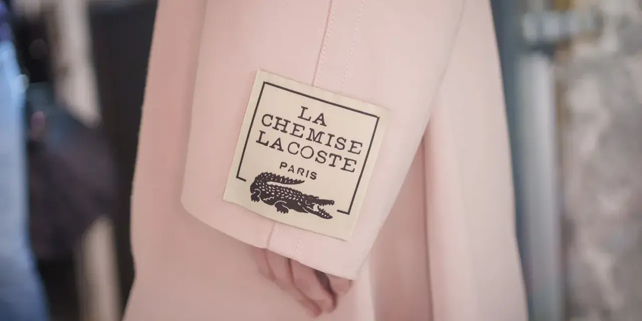 Różowy płaszcz z metką "LA CHEMISE LACOSTE PARIS" z krokodylem, symbol luksusowych marek ubrań.