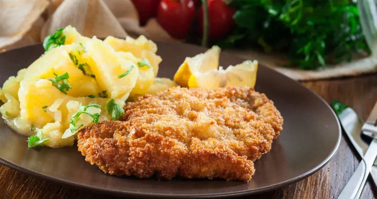 Kotlet schabowy w panierce z ziemniakami i cytryną na brązowym talerzu.