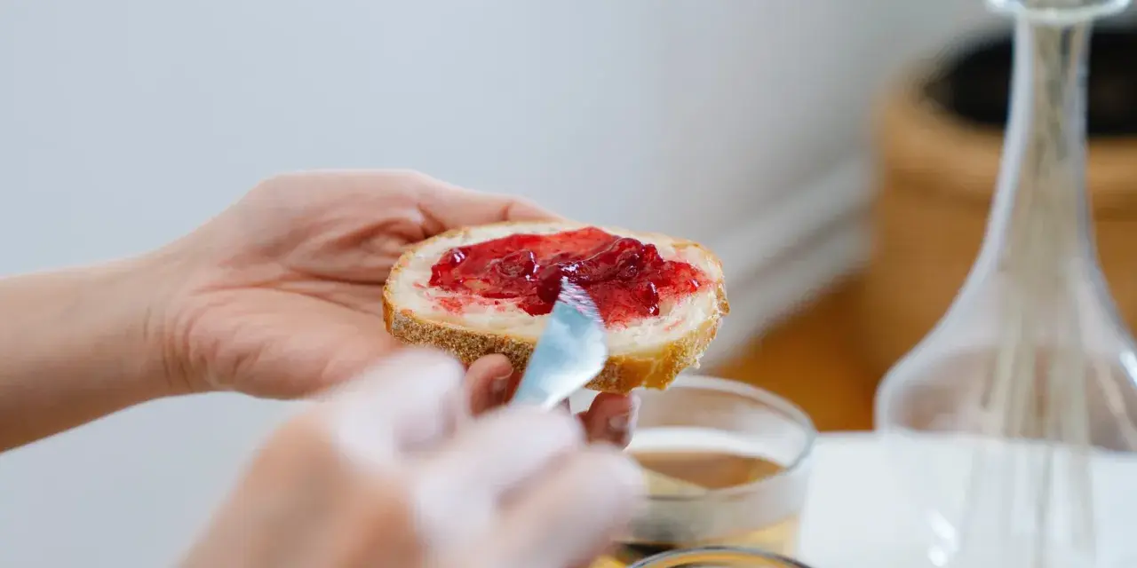 Hände verteilen Marmelade auf Brot. Ein süßer Genuss, der an die besonderen Gelüste in der Schwangerschaft erinnert.