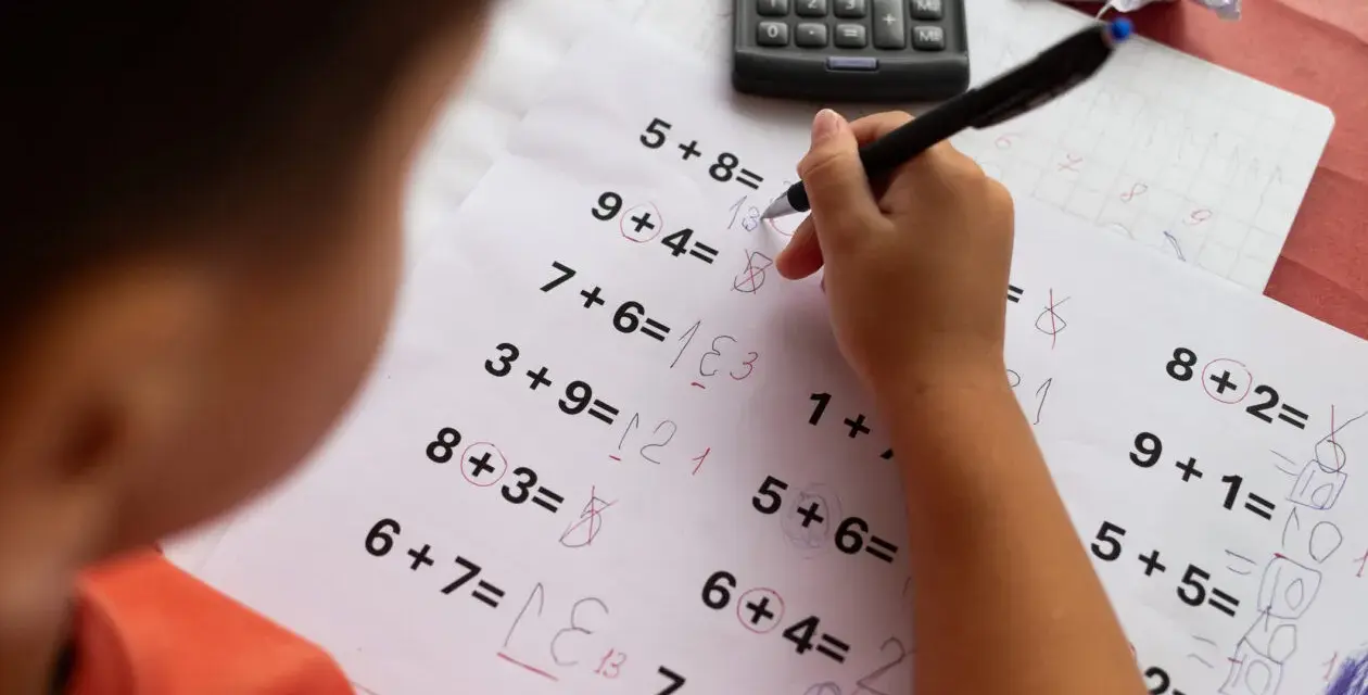 Dziecko zmagające się z zadaniami matematycznymi, być może z dyskalkulią. Widoczne są próby rozwiązań i poprawki.