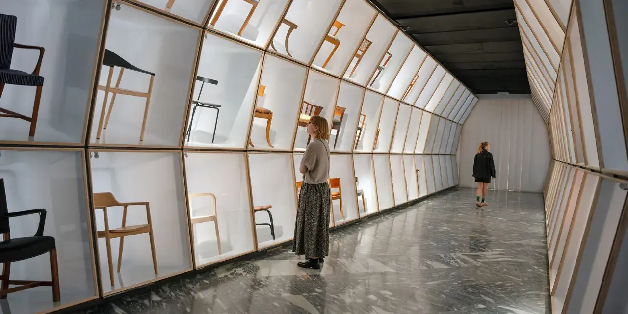 Wystawa krzeseł w muzeum designu Kopenhaga. Ludzie podziwiają ekspozycję w nowoczesnej, geometrycznej przestrzeni.
