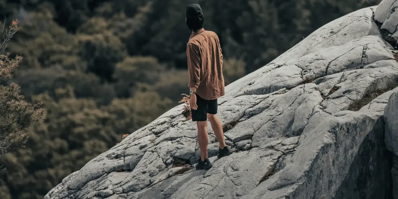 Un homme sur un rocher escarpé, le regard perdu dans le lointain, semble lutter contre sa peur du vide.