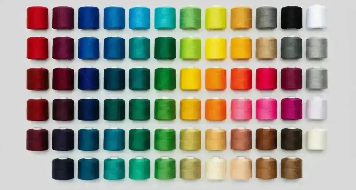 Una gran variedad de tipos de hilos de coser en carretes, organizados por color en filas y columnas.