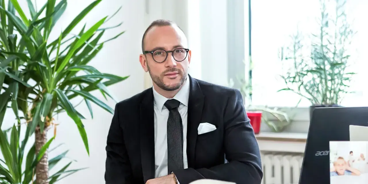 Ein Mann im Anzug sitzt am Schreibtisch, umgeben von Pflanzen. Er ist ein erfahrener Rechtsanwalt für Scheidungsrecht.