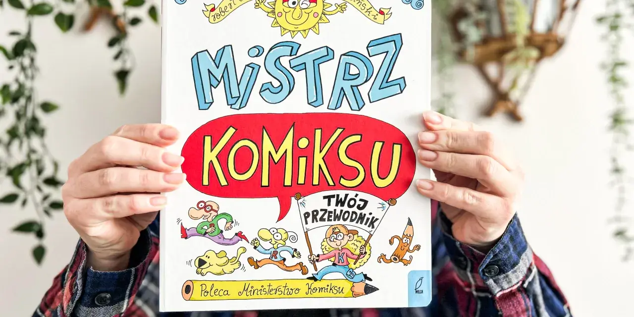 Okładka książki "Mistrz Komiksu" z rysunkami postaci i słońca, trzymana przez ręce.