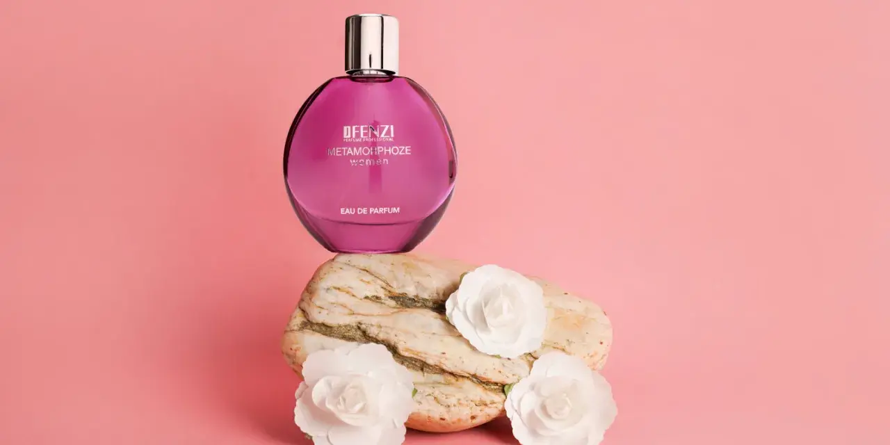 Różowa butelka perfum JFenzi Mon Amie Metamorphoze Women na kamieniu z białymi kwiatami.