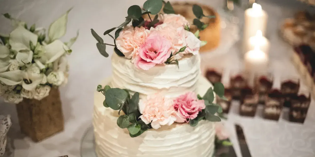 Elegancki tort weselny z kremową dekoracją i pastelowymi kwiatami, ozdobiony gałązkami eukaliptusa.