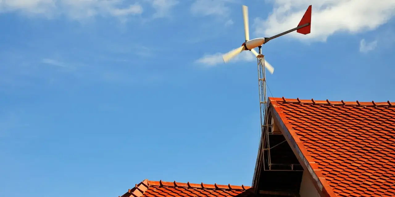 Mała elektrownia przydomowa na tle błękitnego nieba z chmurami. Wirnik turbiny wiatrowej obraca się, dostarczając czystą energię.
