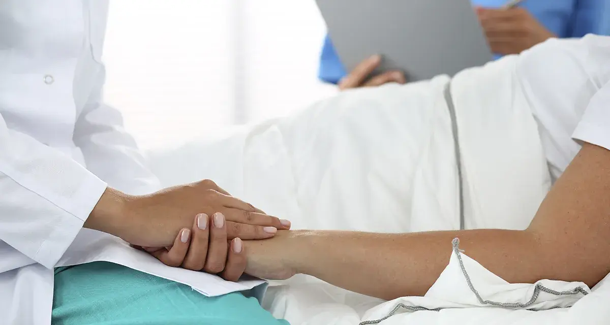 Lekarz w białym kitlu trzyma dłoń pacjenta, który leży w łóżku. To pokazuje, jaki lekarz nie może poślubić swojej pacjentki.