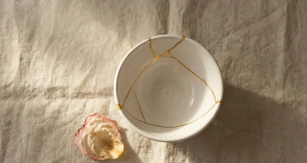 Biała miska z pęknięciami zespolonymi złotem, jak w kintsugi, obok zasuszonego płatka róży. Symbolizuje proces leczenia, jak w przypadku osobowości borderline test.