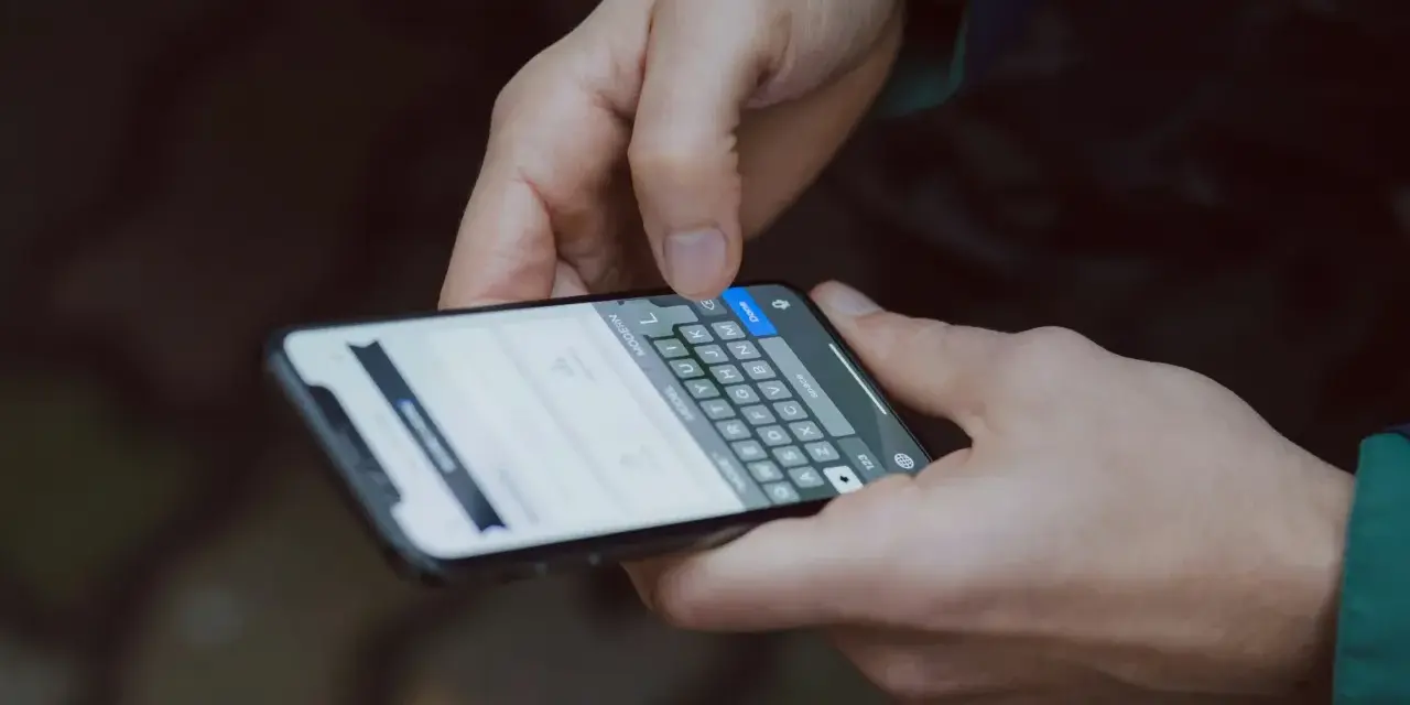 Dłonie trzymają smartfon z klawiaturą. Dowiedz się, jak wydrukować zdjęcie z telefonu, by zachować wspomnienia.