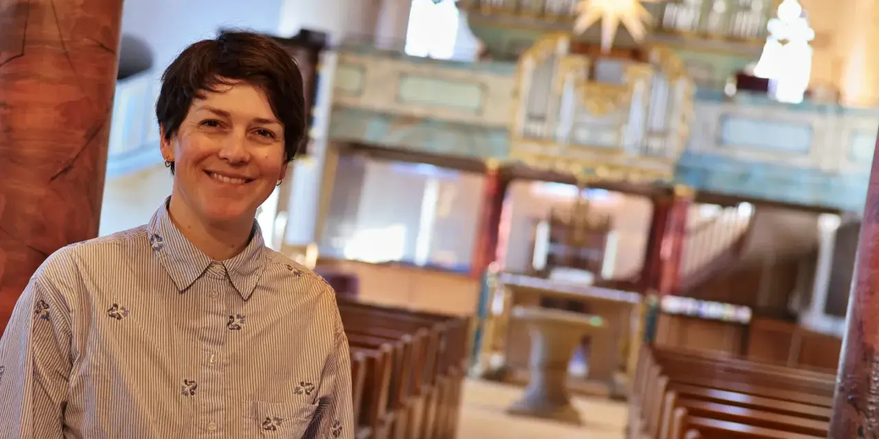 Eine lächelnde evangelische Pfarrerin steht in einer Kirche vor einer Orgel.