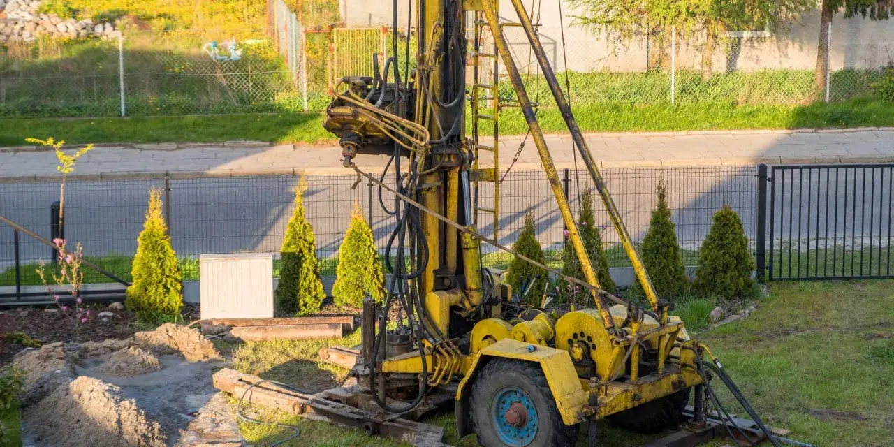 Żółta wiertnica na placu budowy. Rozpoczynają się prace nad studnią głębinową, koszt inwestycji zależy od wielu czynników.