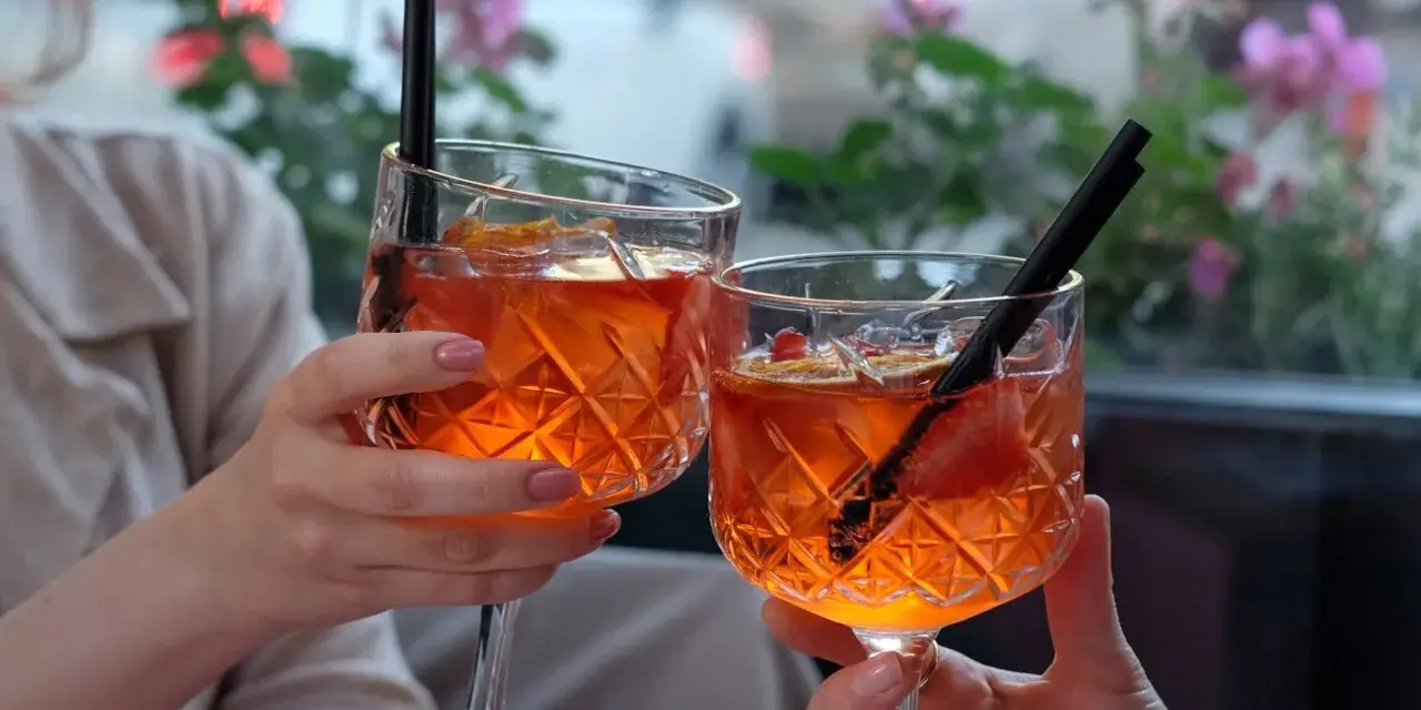 Dwie osoby wznoszą toast Aperolem. Orzeźwiający drink z pomarańczą i truskawką.