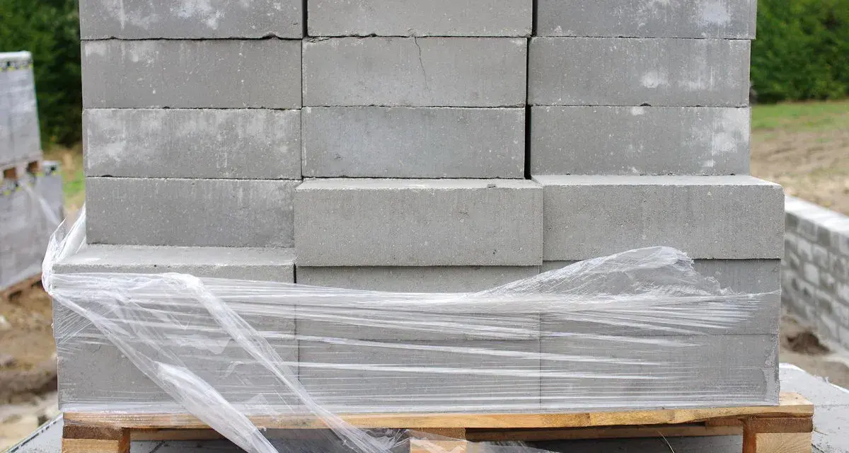 Stos betonowych bloczków fundamentowych na palecie, owiniętych folią.