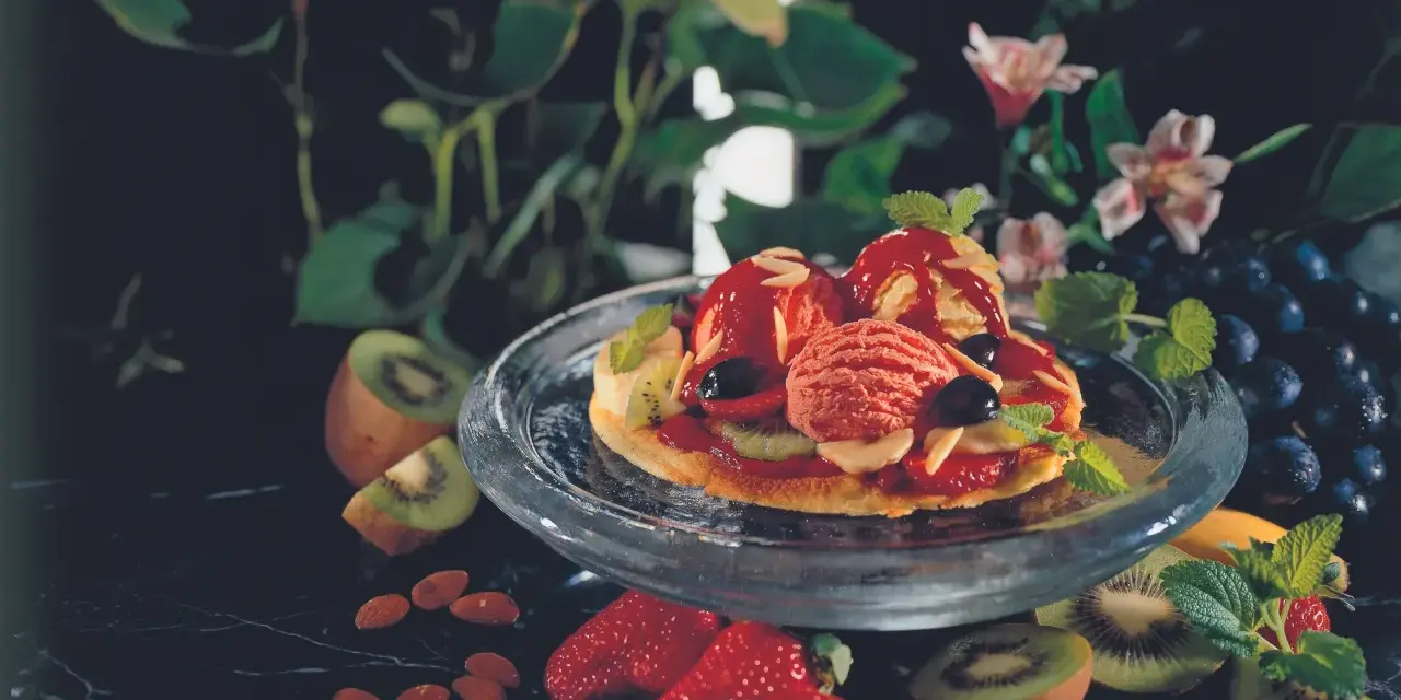 Eine süße Pizza mit Eis, Beeren und Kiwi. Mandeln und Trauben garnieren das Dessert.